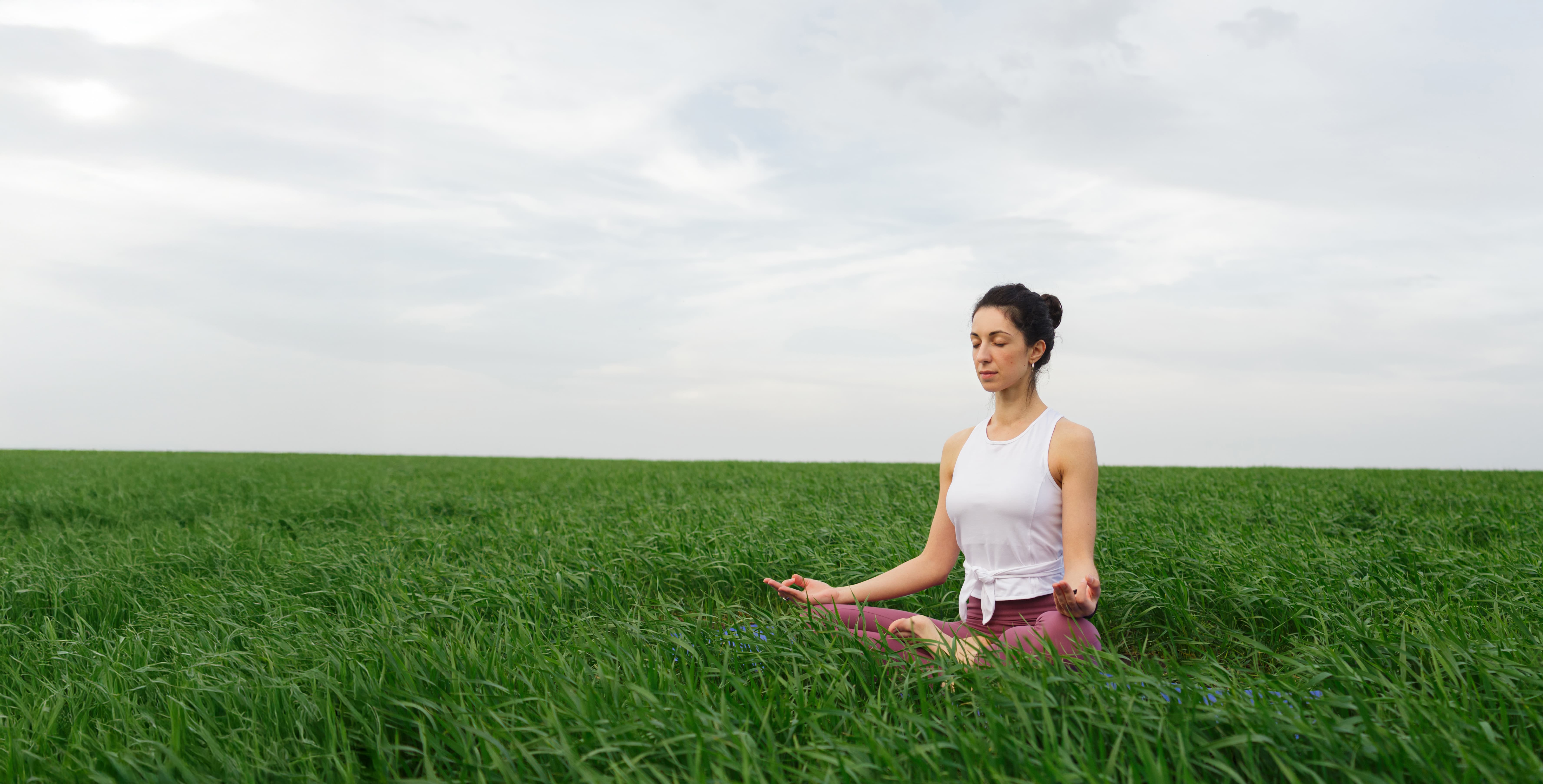 young slim girl doing yoga outdoors green field