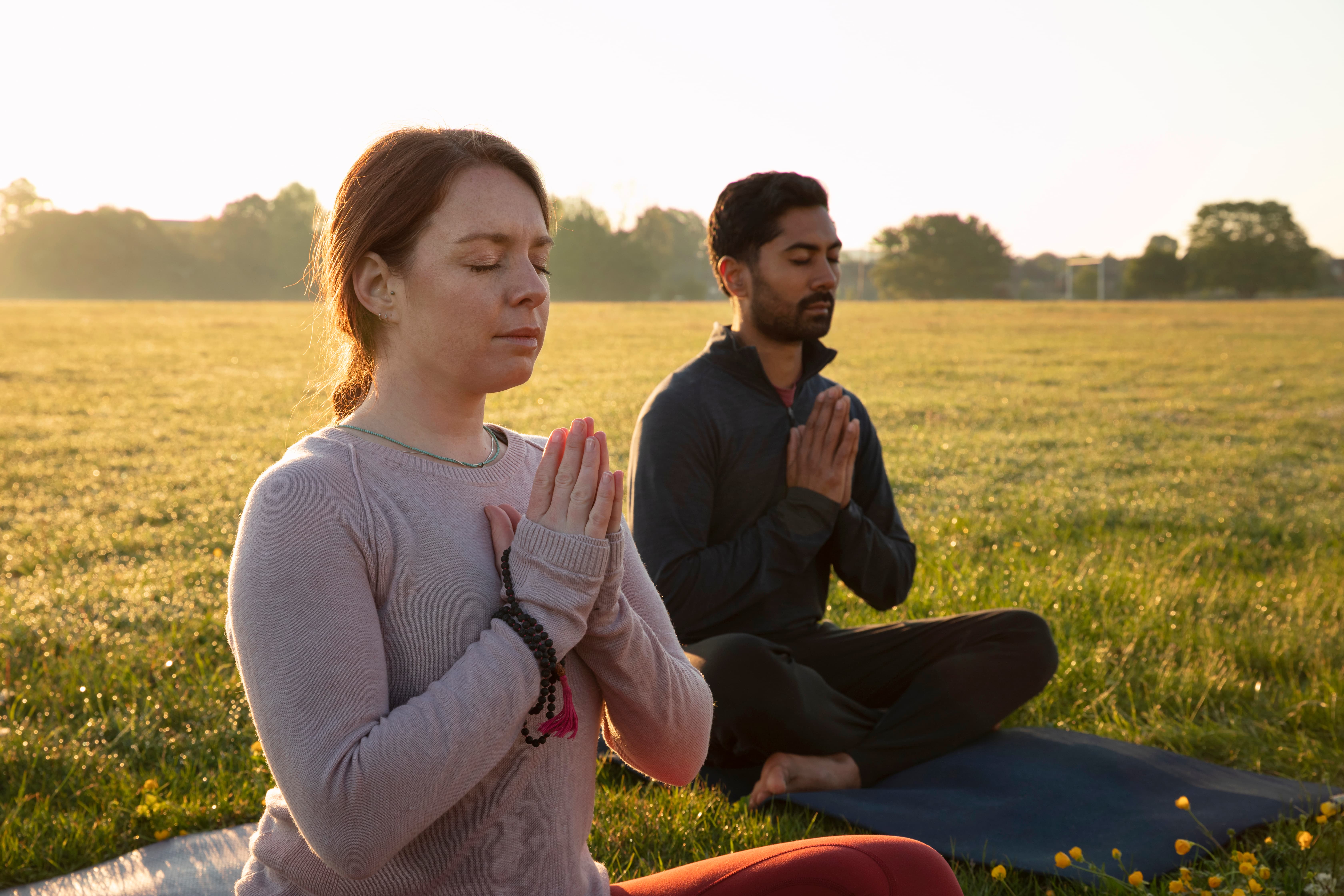a side view of a man and a woman are meditating in outdoors