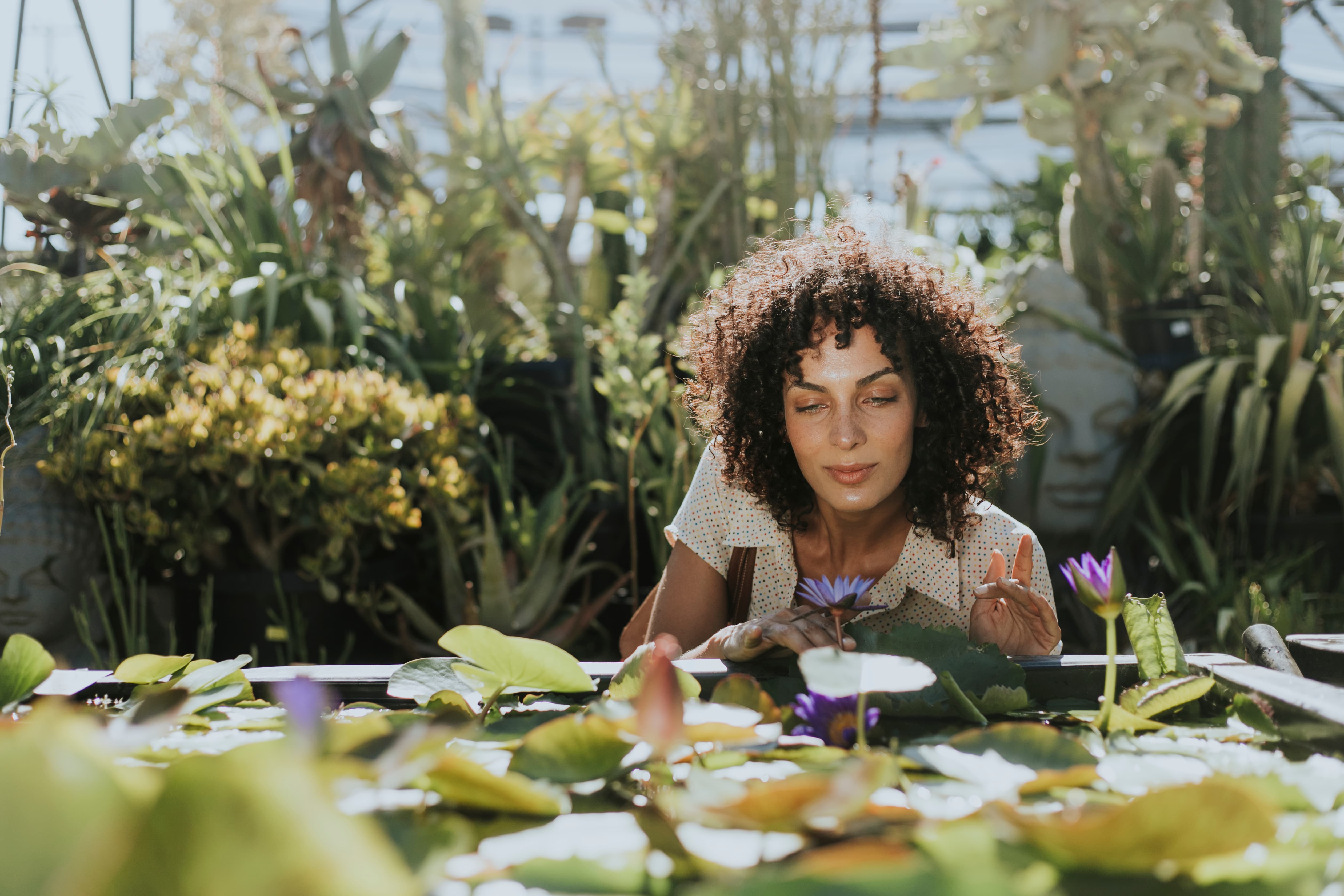 a beautiful woman picking up a flower by a lotus pond