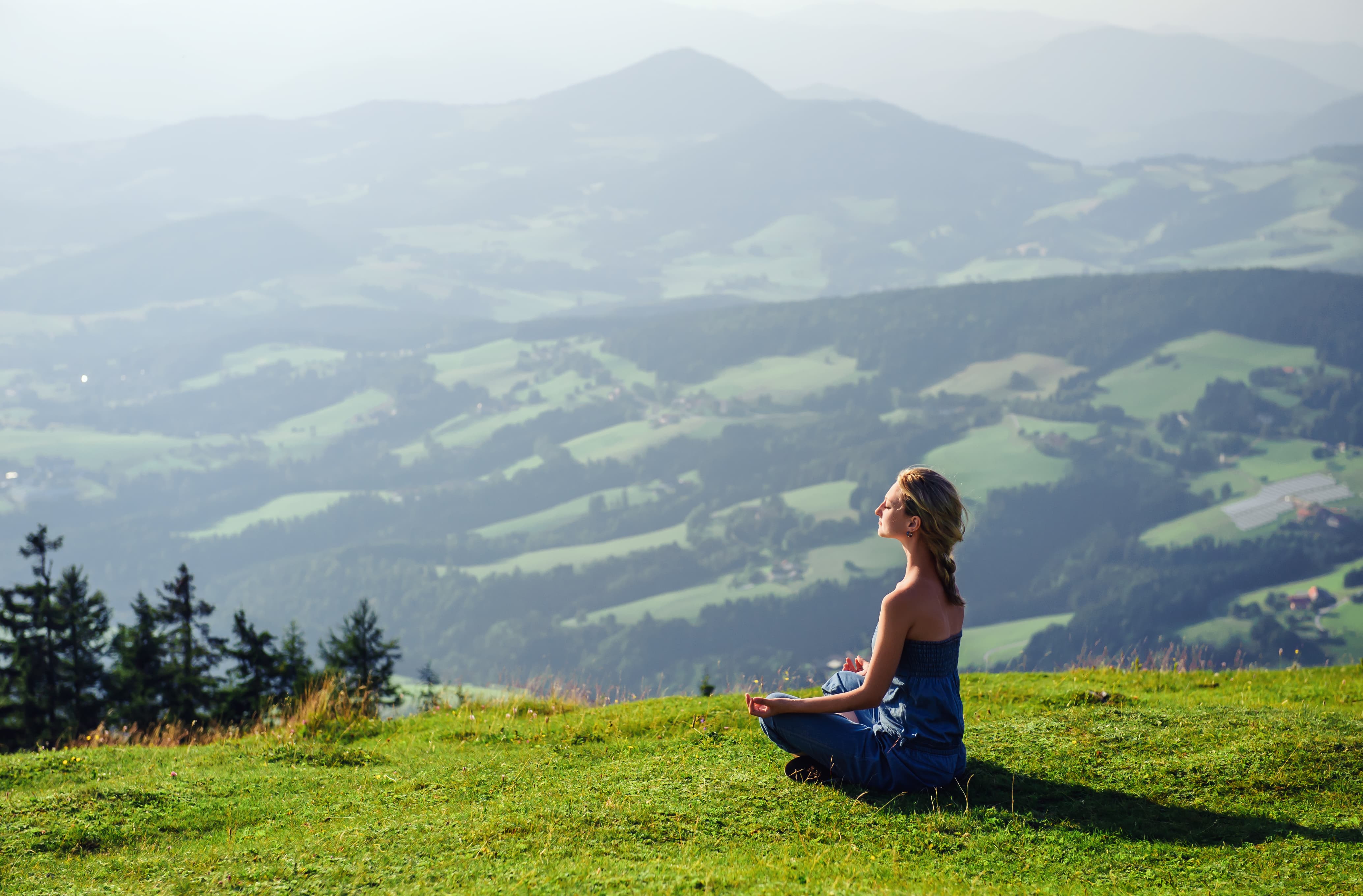 a woman is meditating on a grass mountain