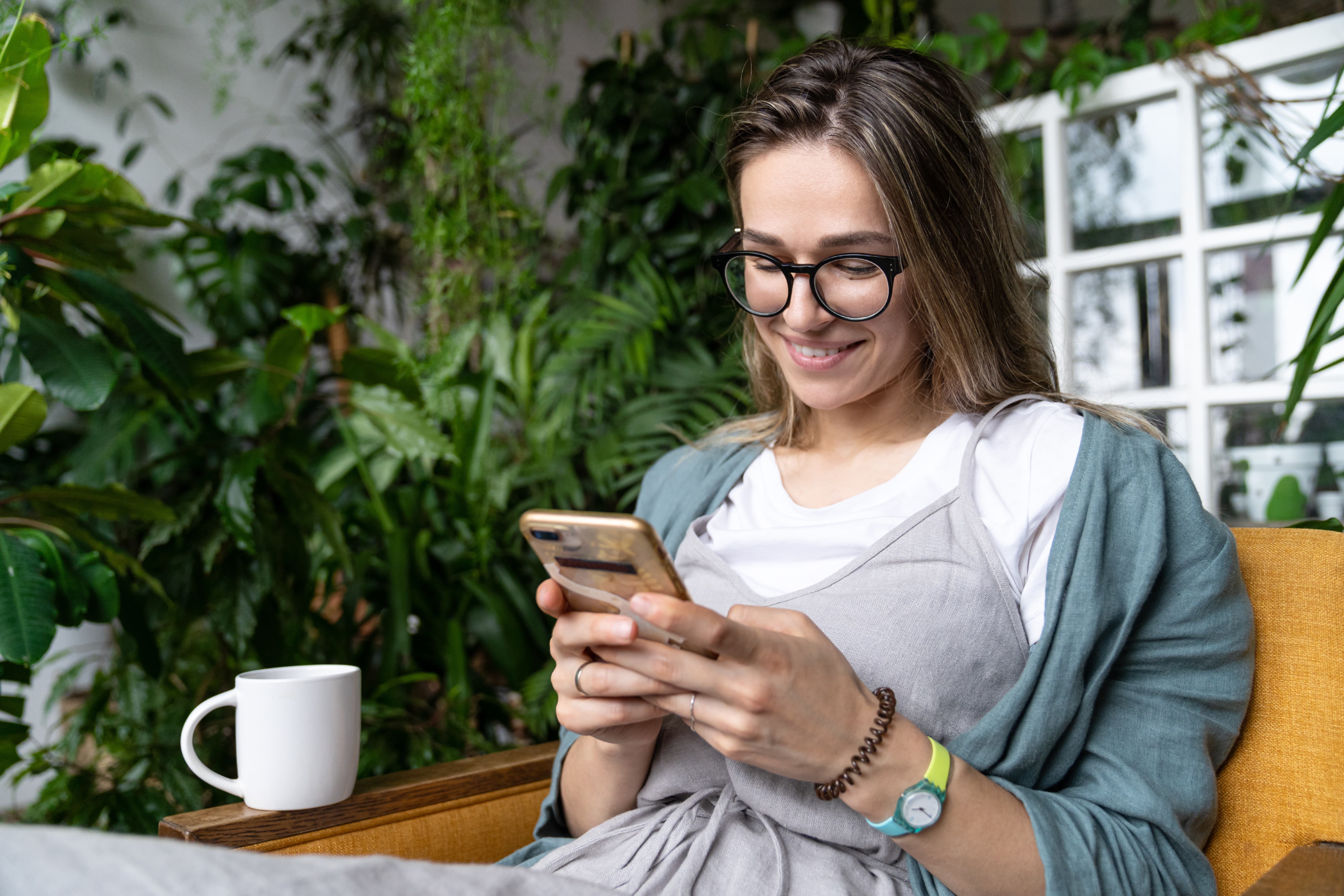 a smiling woman is using her smart phone sitting home